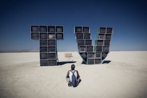 Man looking at a sculpture spelling TV made out of TVs