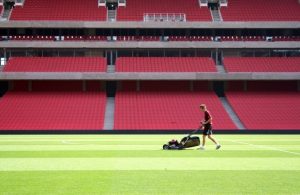 Photo of a person mowing the green lawn inside a sports arena