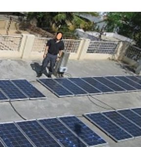 Photograph of a person standing on a rooftop in front of many solar panels