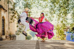 A man and woman wearing traditional Mexican clothing are dancing in the street.