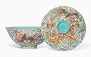 Photograph of a ceramic bowl with an exquisite pattern of a dragon and waves, with a lid with the same pattern. The inside of the bowl appears to be plain turquoise, as is the top circular handle of the lid.