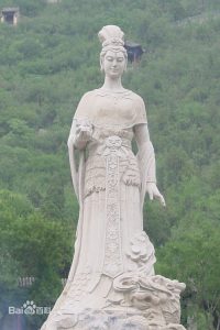 Photograph of a white stone statue of a women with tighter fitting long robes. There is no indication of her having a snake body.