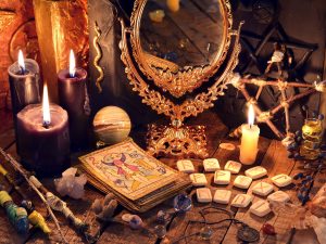 A photograph of a very crowded table, with candles, tarot cards, a mirror, tiles, a pentagram
