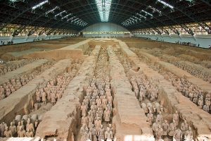 Photograph shows pit No. 1 with long rows of soldiers excavated, under a large modern roof.