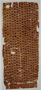 Photograph shows a piece of yellow-brown silk with vertical lines of characters. They are demarcated by red lines, marking the columns.
